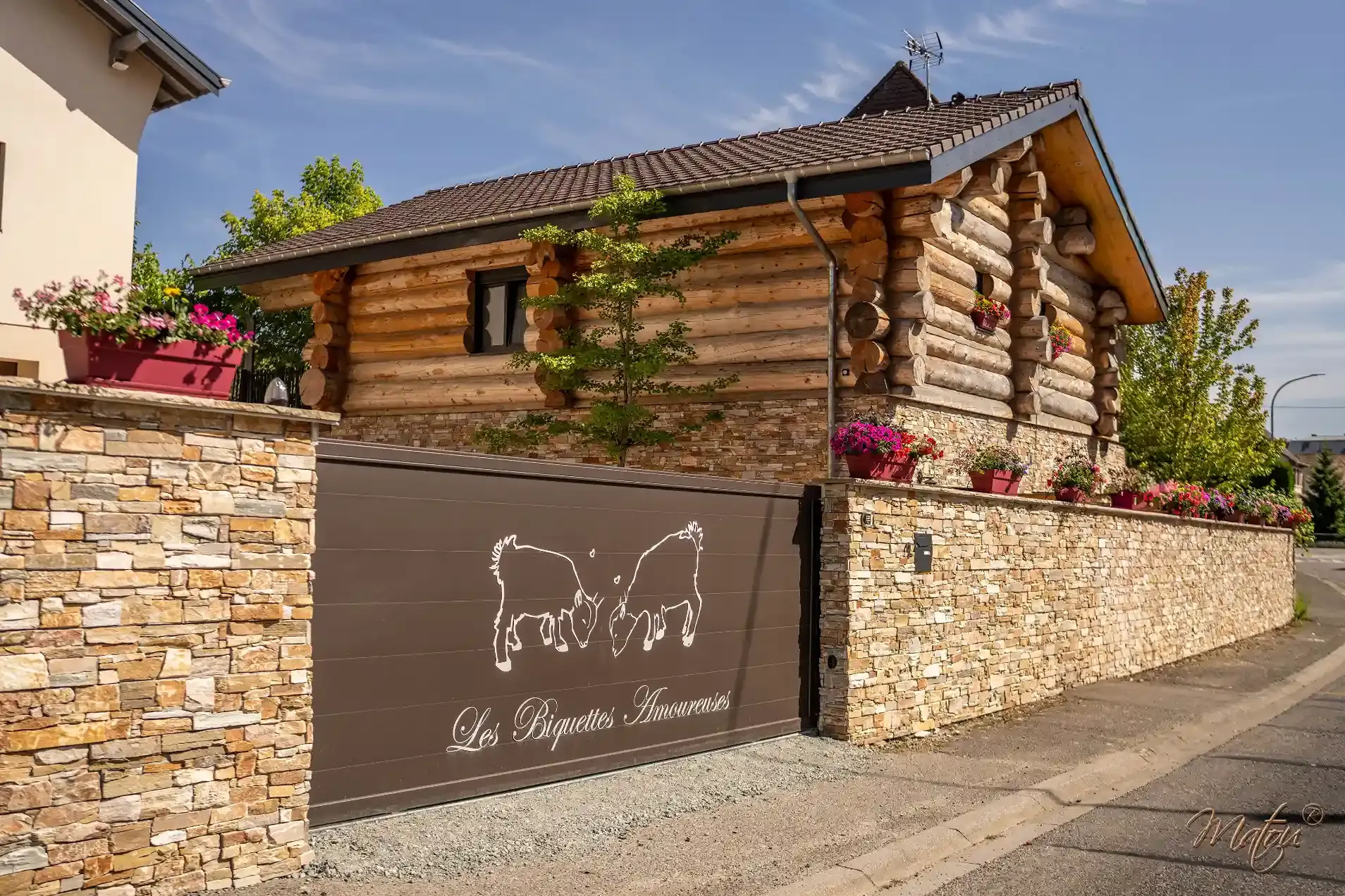 Portail d’entrée des Biquettes Amoureuses devant un chalet en bois à Carspach