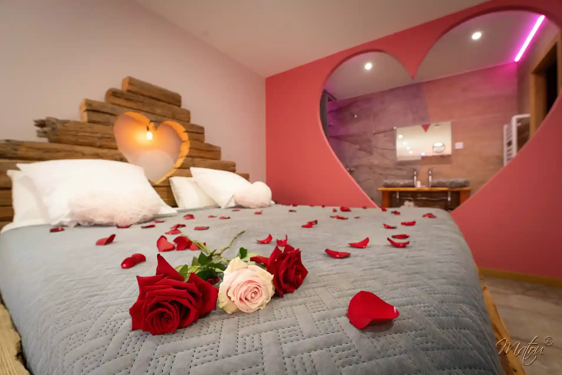 Lit décoré de roses avec vue sur le jacuzzi privatif de la love room Bisou Sucré